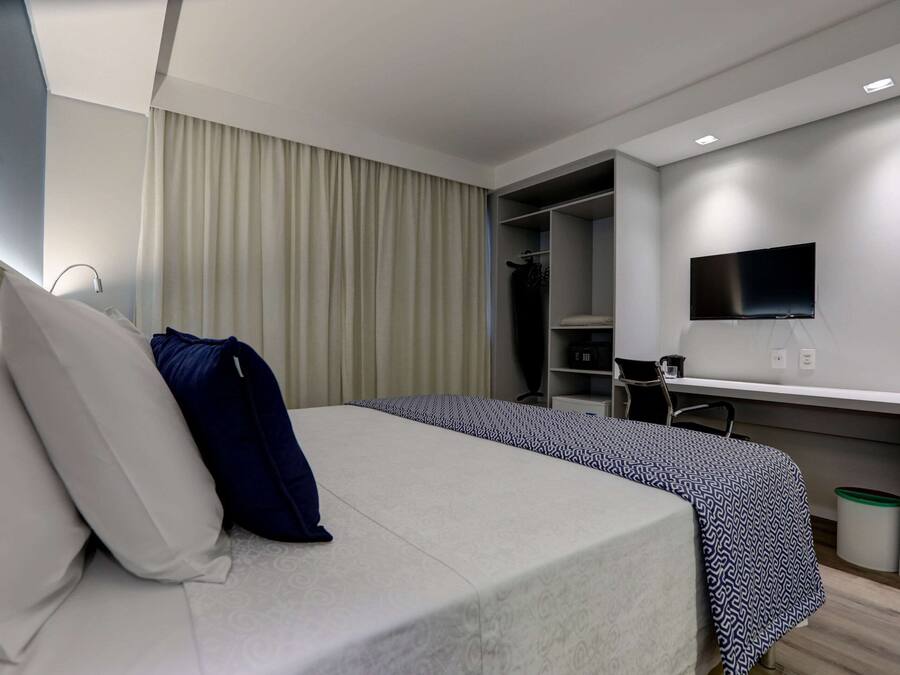 A modern hotel room with a bed, a desk, a TV, and a wardrobe.