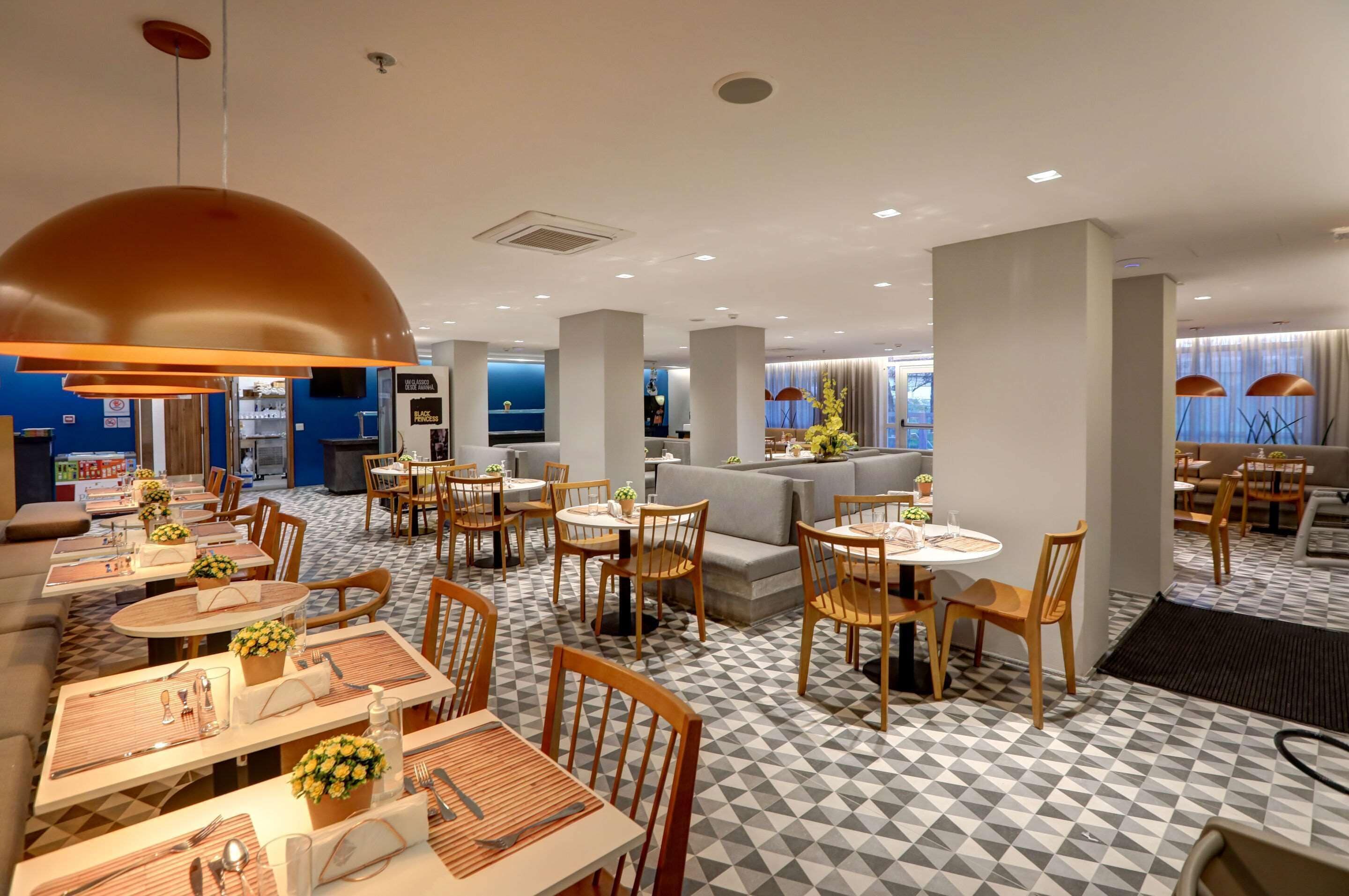 A modern hotel lobby with round tables, wooden chairs, and a check-in counter.