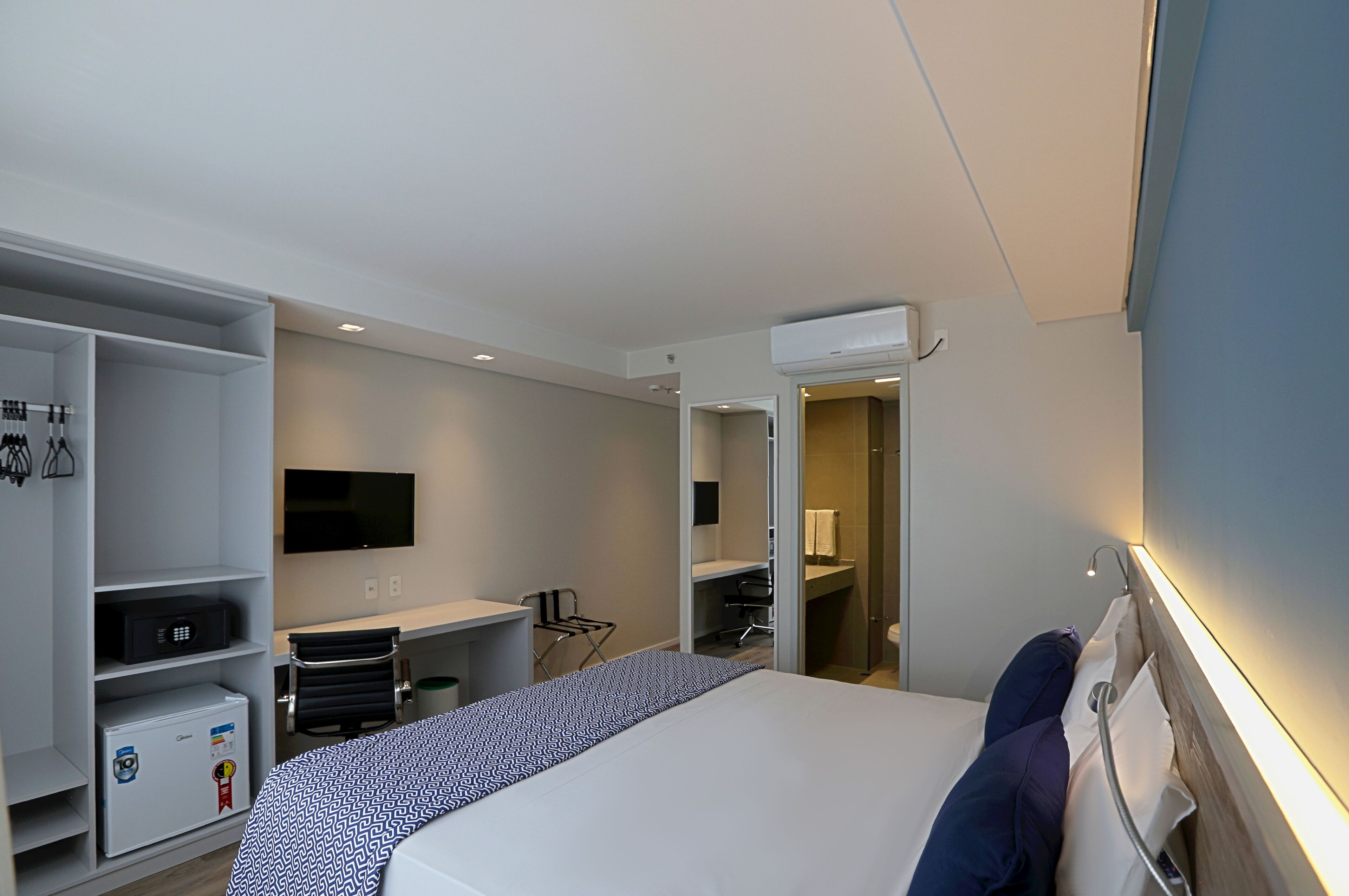 A modern hotel room with a bed, a desk, a chair, a TV, and a wardrobe.