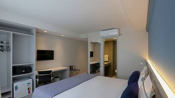 A modern hotel room with a bed, a desk, a chair, a TV, and a wardrobe.