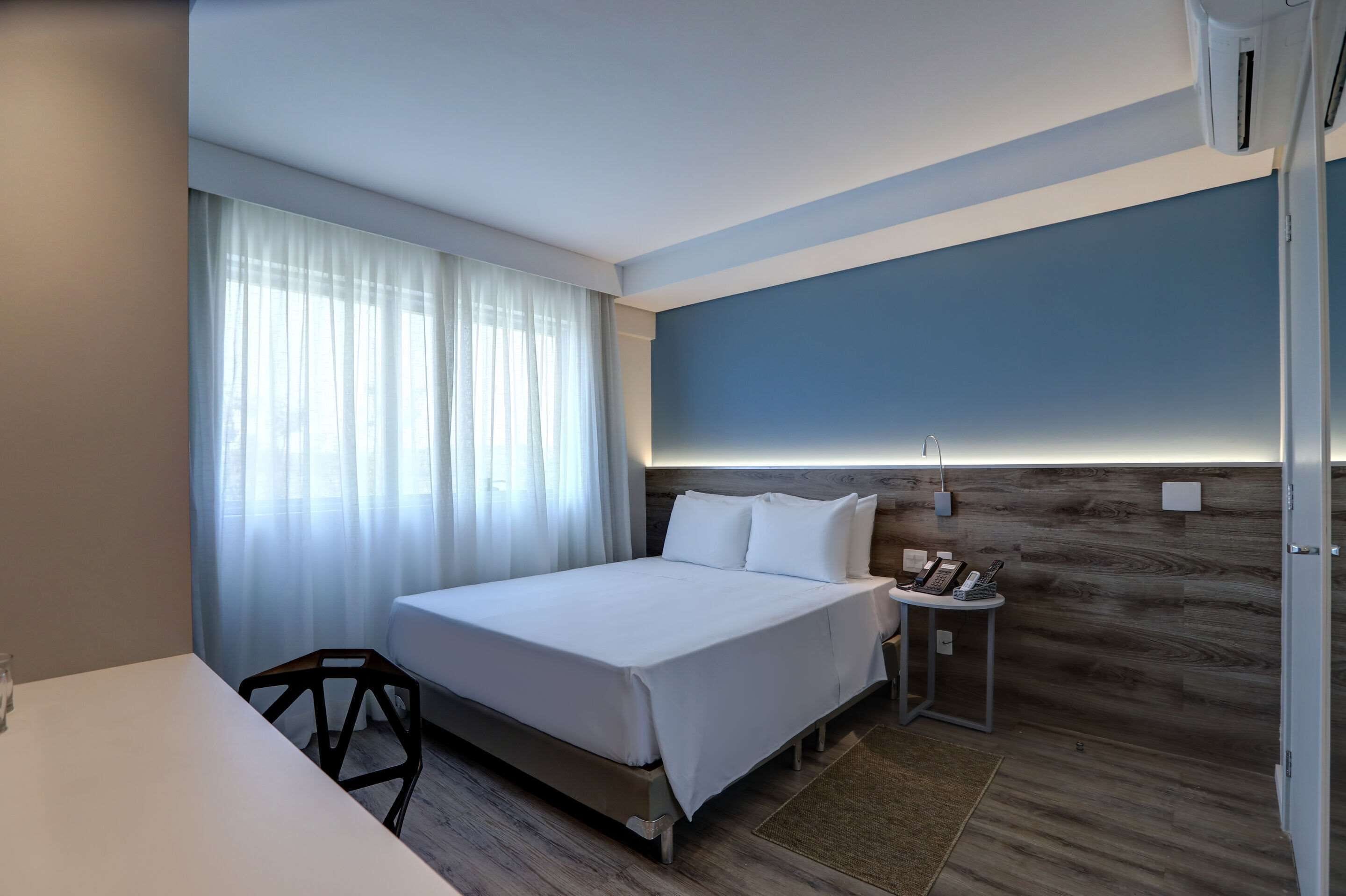 Una habitación de hotel moderna con una cama grande, una mesita de noche con teléfono y una pared de acento de madera.