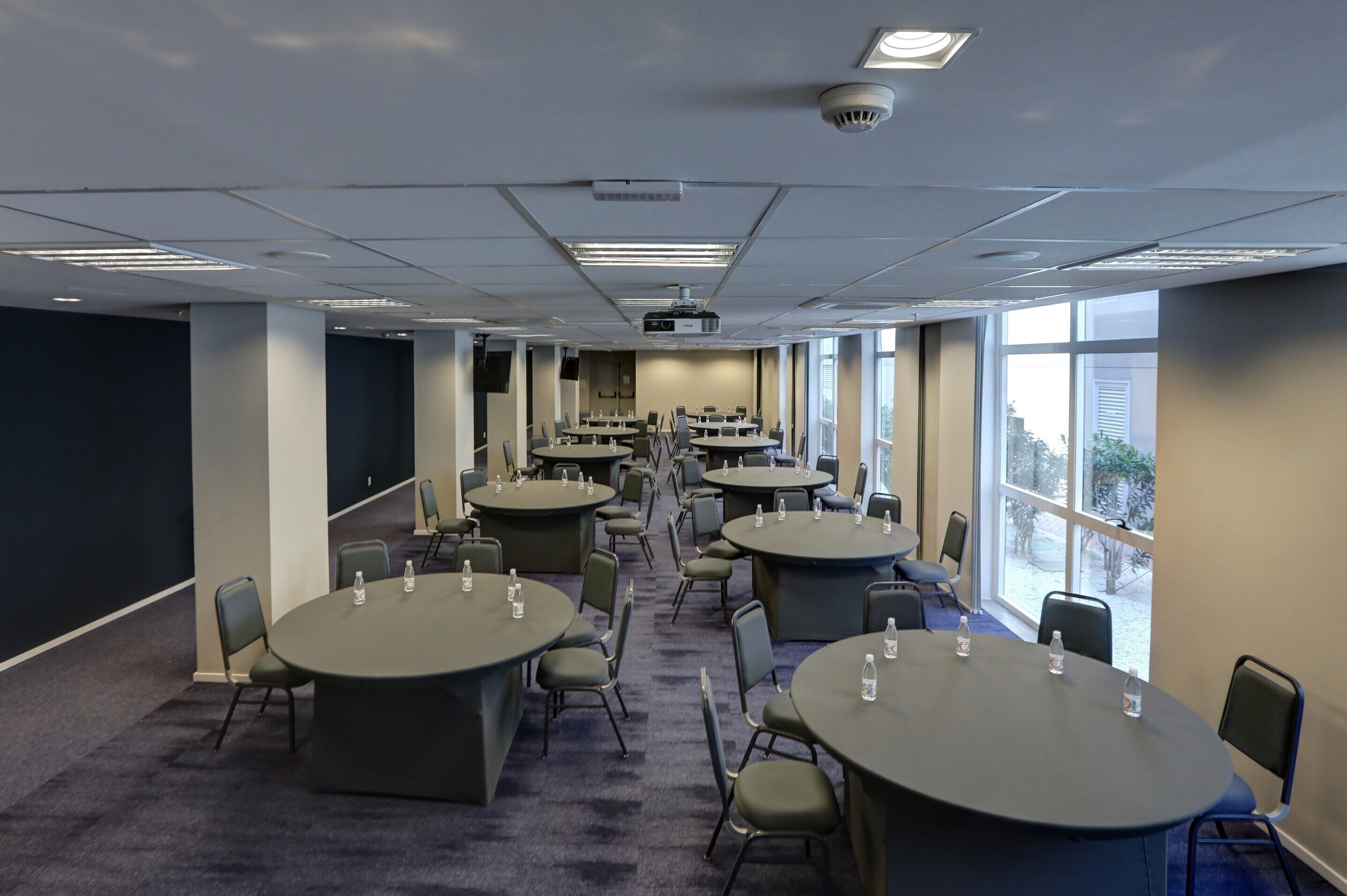 A conference room with multiple tables and chairs, a projector, and large windows.
