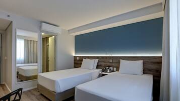 A hotel room with two single beds, a small bedside table with a phone, and a mirror.