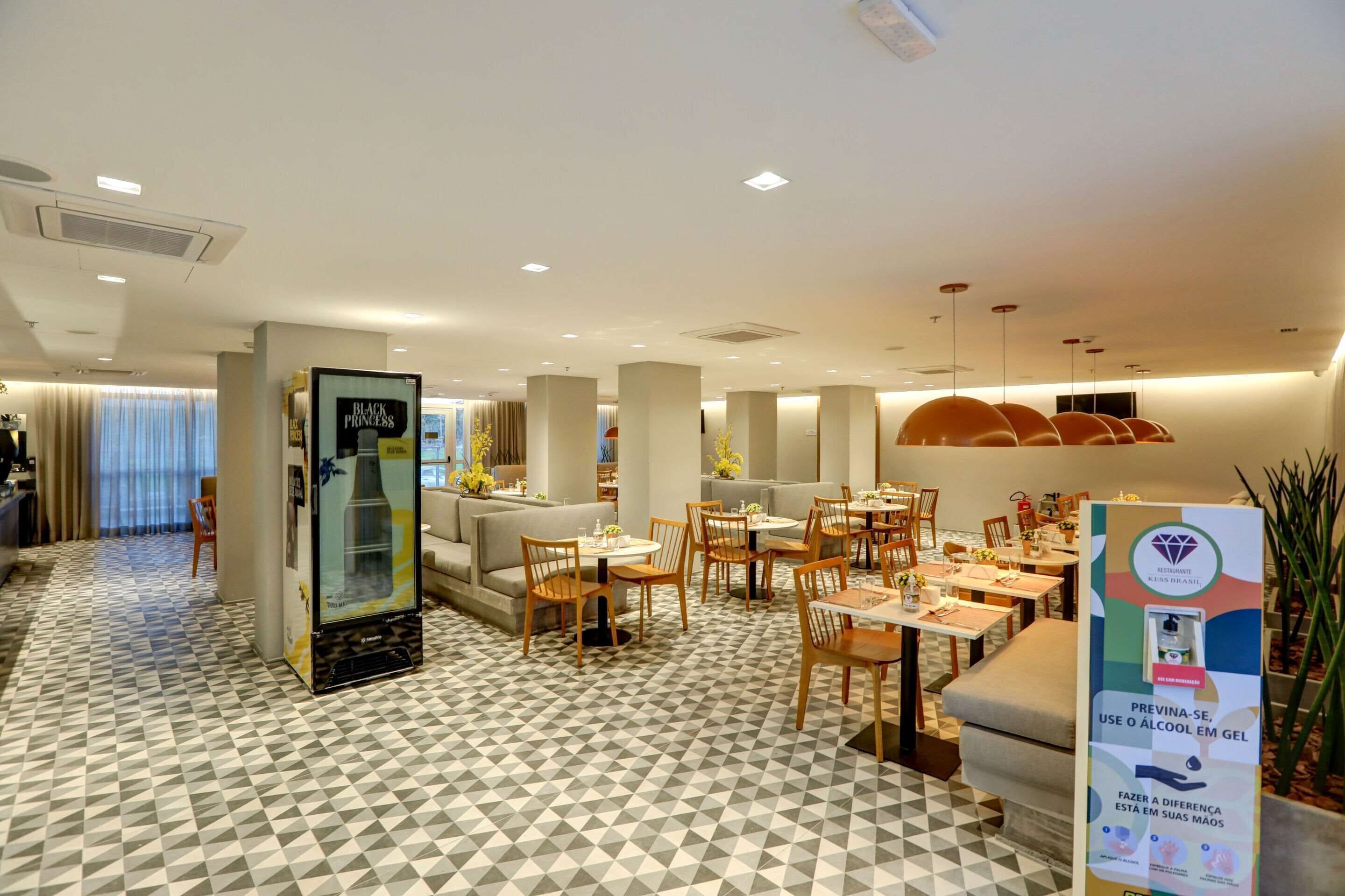 Un vestíbulo de hotel con suelo de estampado geométrico, un quiosco de autoservicio y una zona de estar con mesas y sillas.
