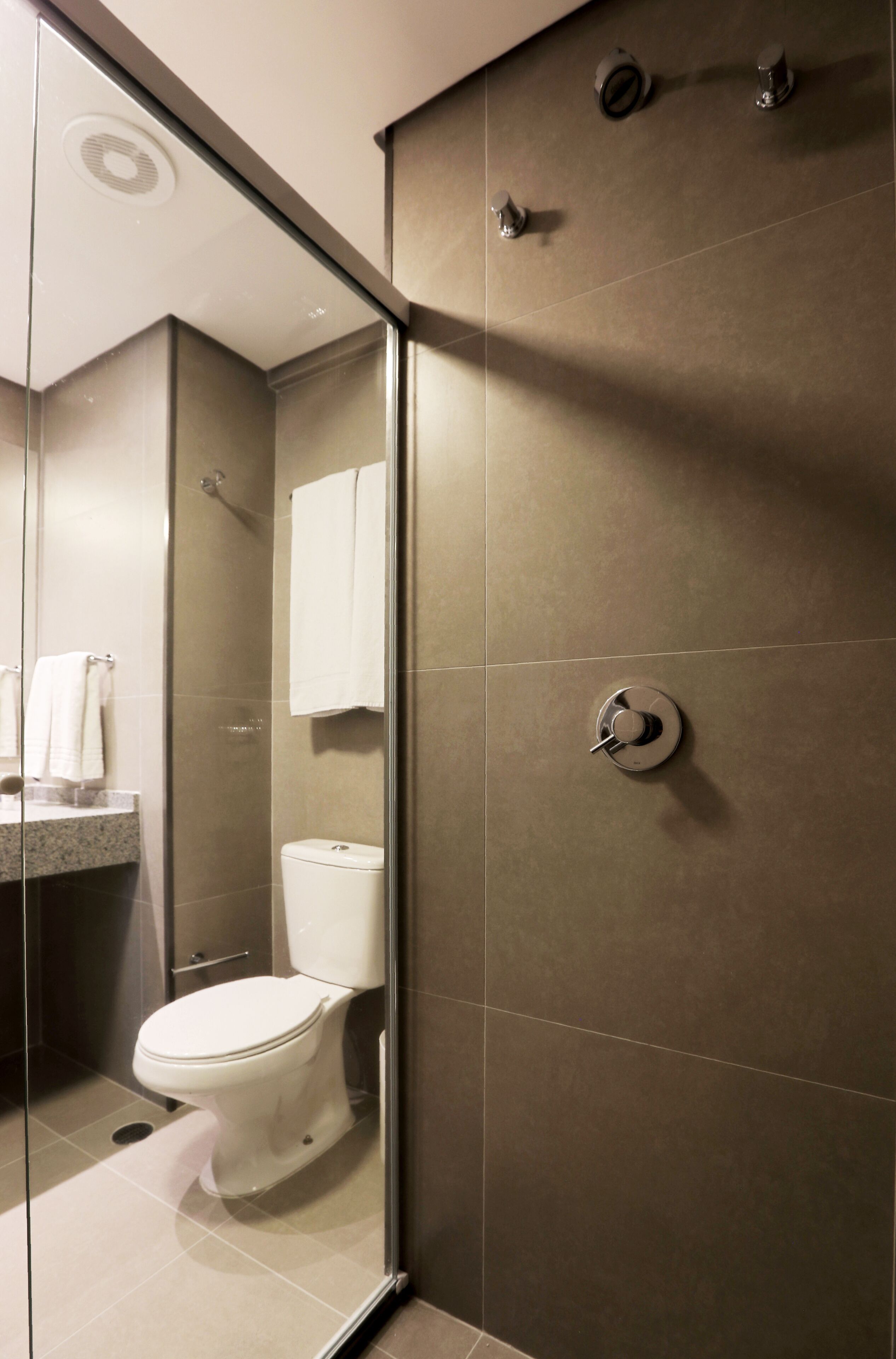Een moderne badkamer met een douchecabine van glas, een toilet en een wastafel met een marmeren aanrechtblad.