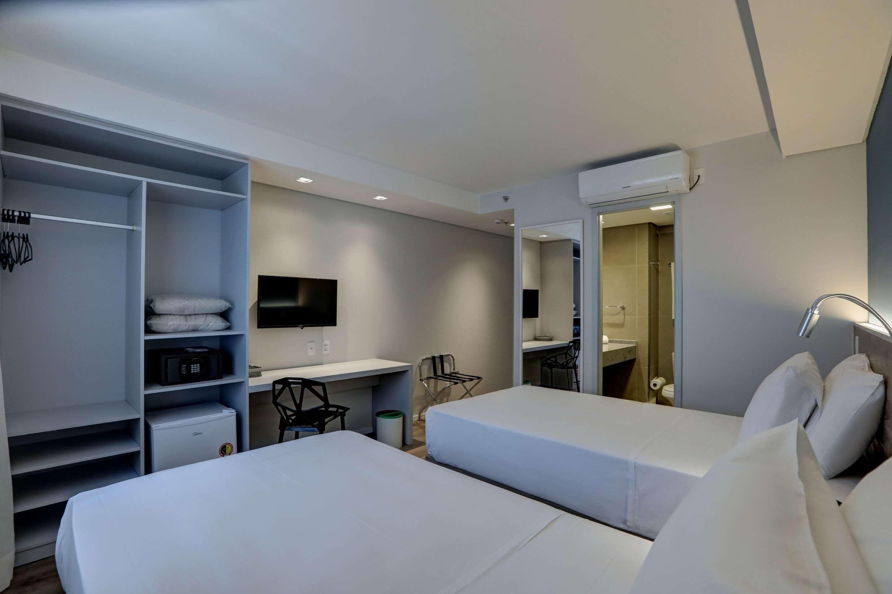 Habitación de hotel con dos camas, un escritorio con silla, un televisor y un armario.