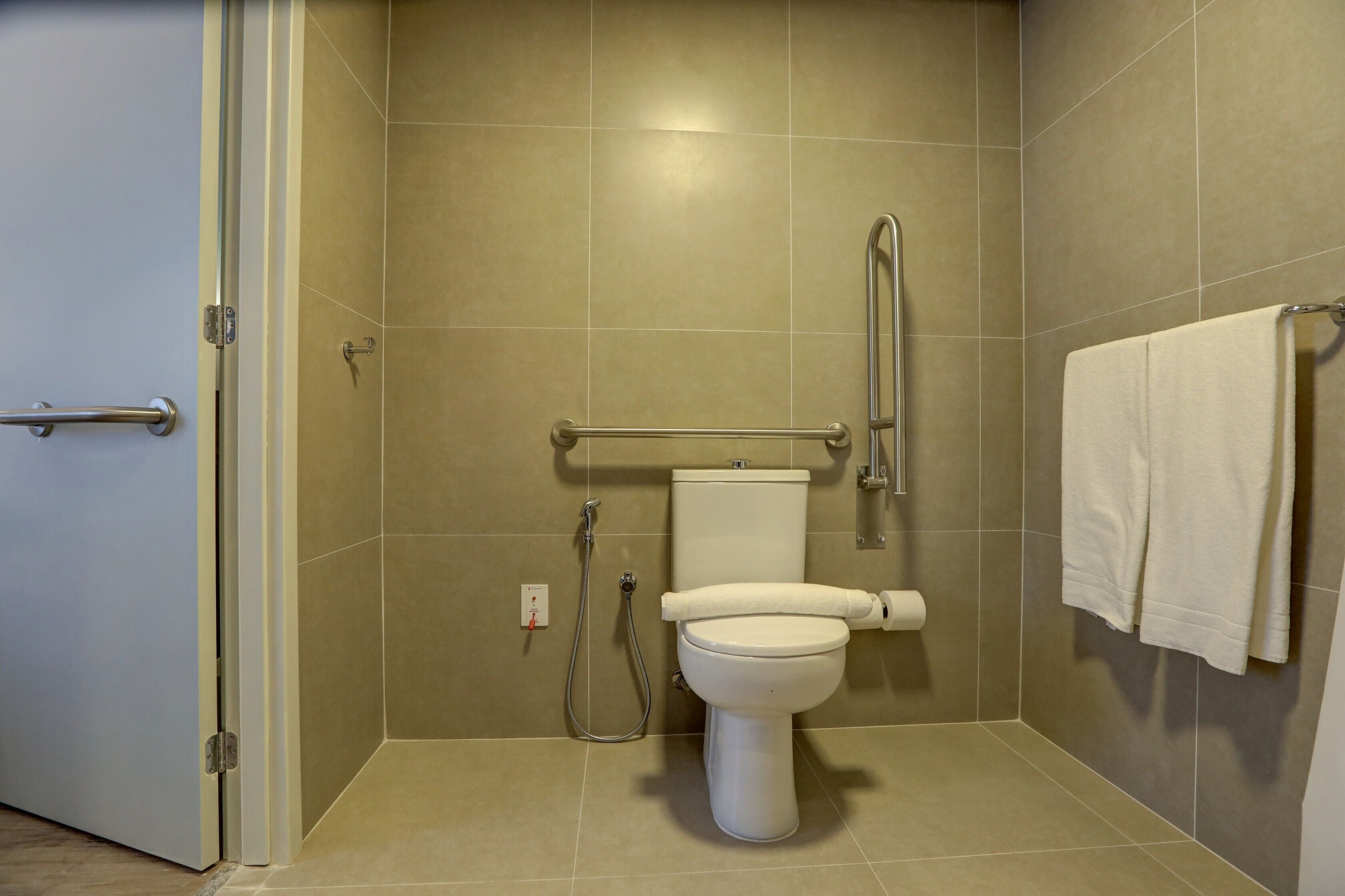 A bathroom with a toilet, grab bars, a shower area, and a towel rack.