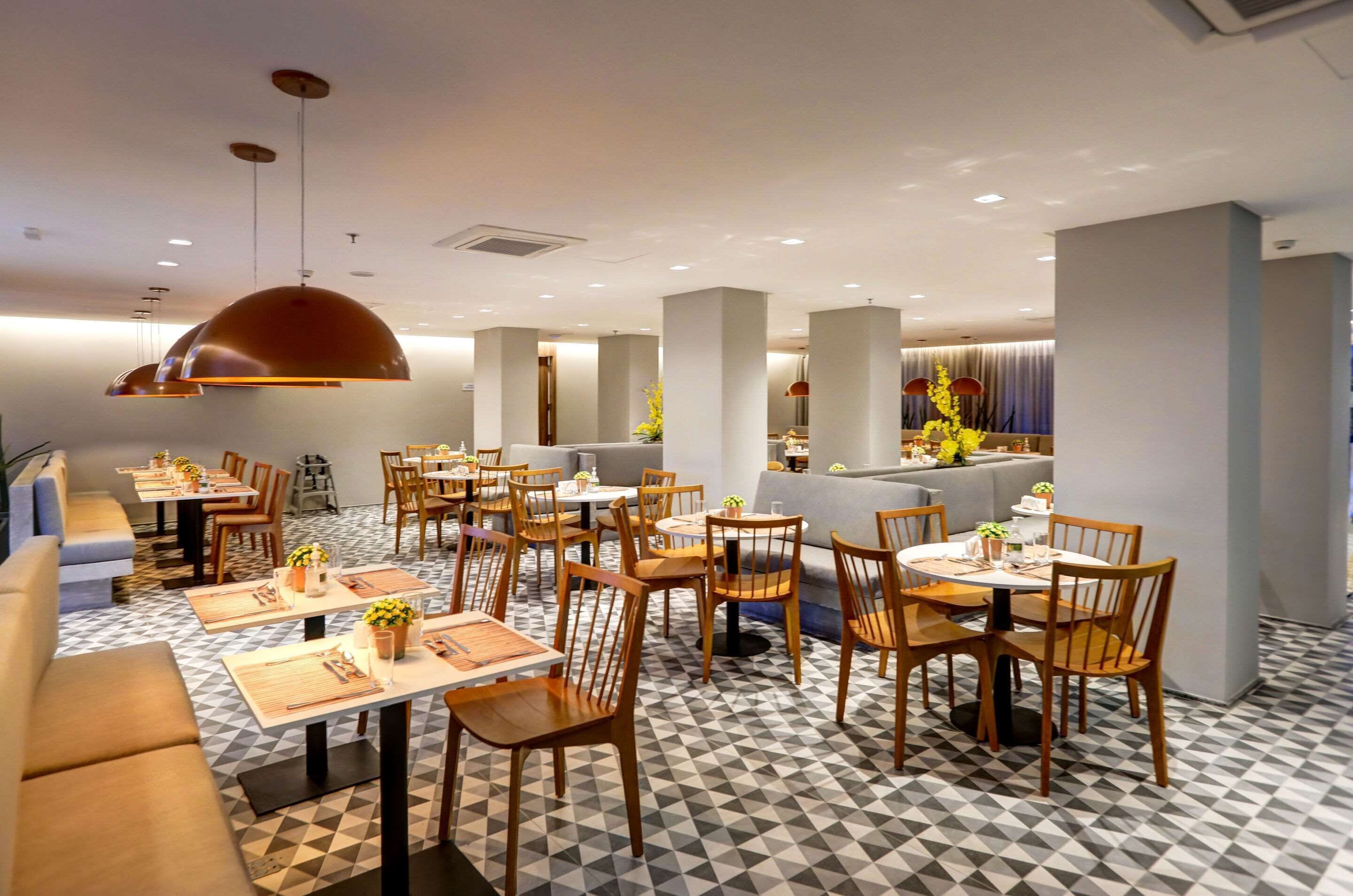 A modern restaurant with a geometric patterned floor, wooden tables and chairs, and pendant lighting.