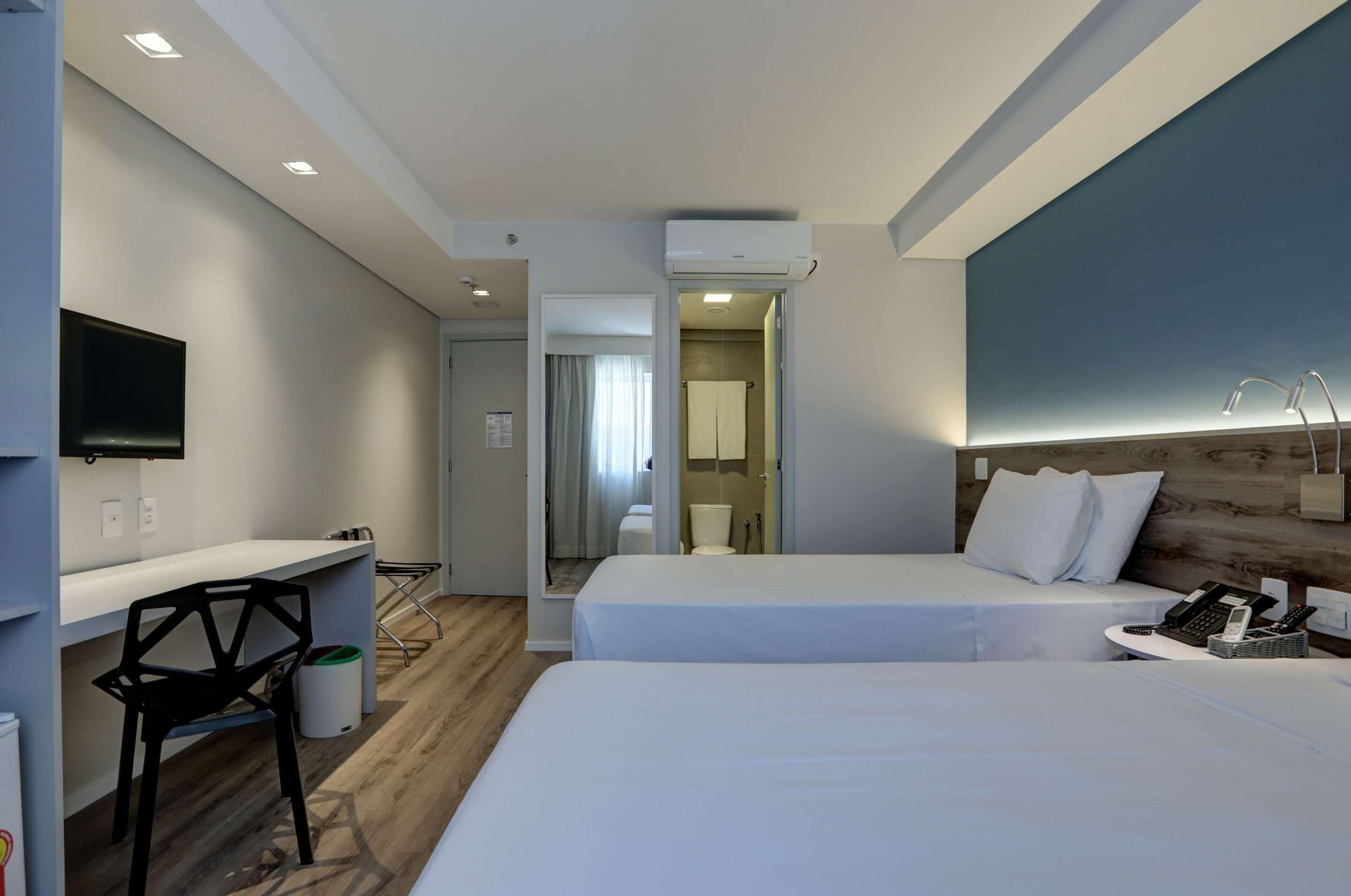 Een hotelkamer met twee bedden, een bureau, een stoel, een televisie en een badkamer die door een open deur zichtbaar is.
