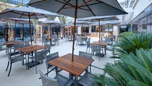 An outdoor patio area with tables and chairs, large umbrellas, and a view of a modern building. - Comfort Hotel Guarulhos - Aeroporto (Guarulhos)
