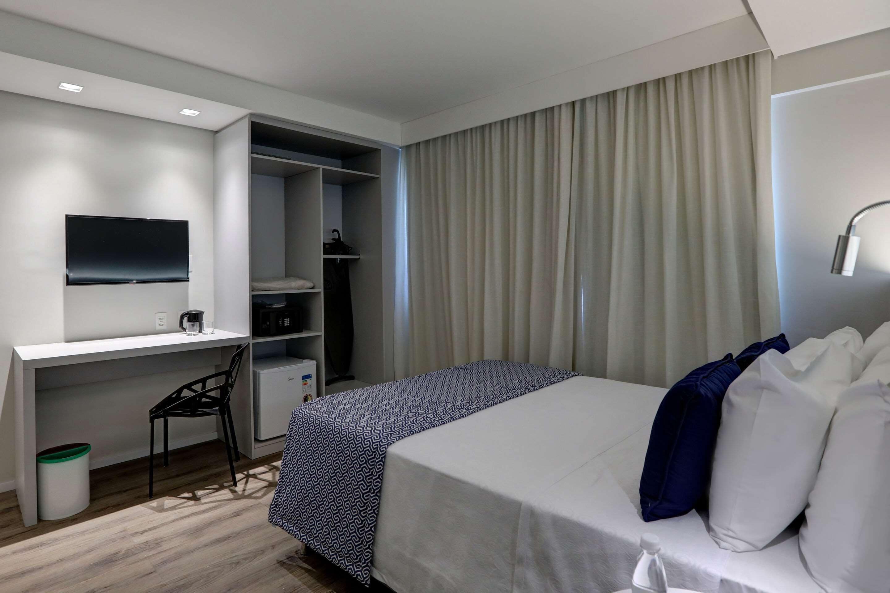 A hotel room with a bed, a desk with a chair, a television, a wardrobe, and a bathroom.