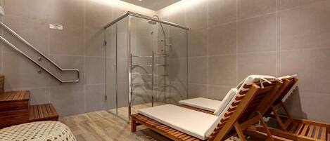 Un baño moderno con cabina de ducha de vidrio, sillones de madera y un banco de madera.