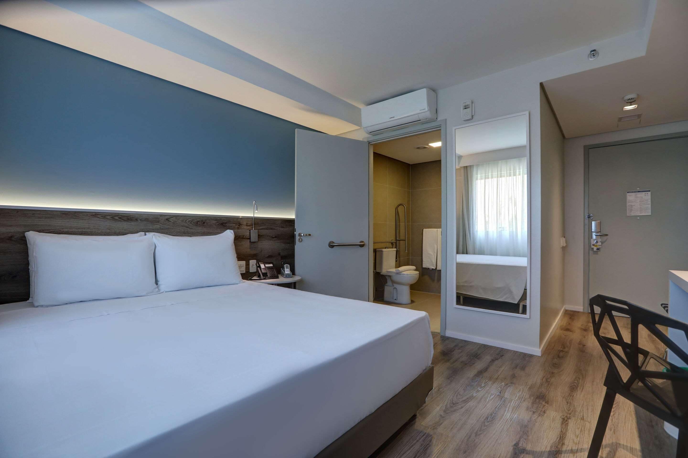 Una camera d'albergo con un letto grande, una scrivania e un bagno visibile tramite una porta aperta.