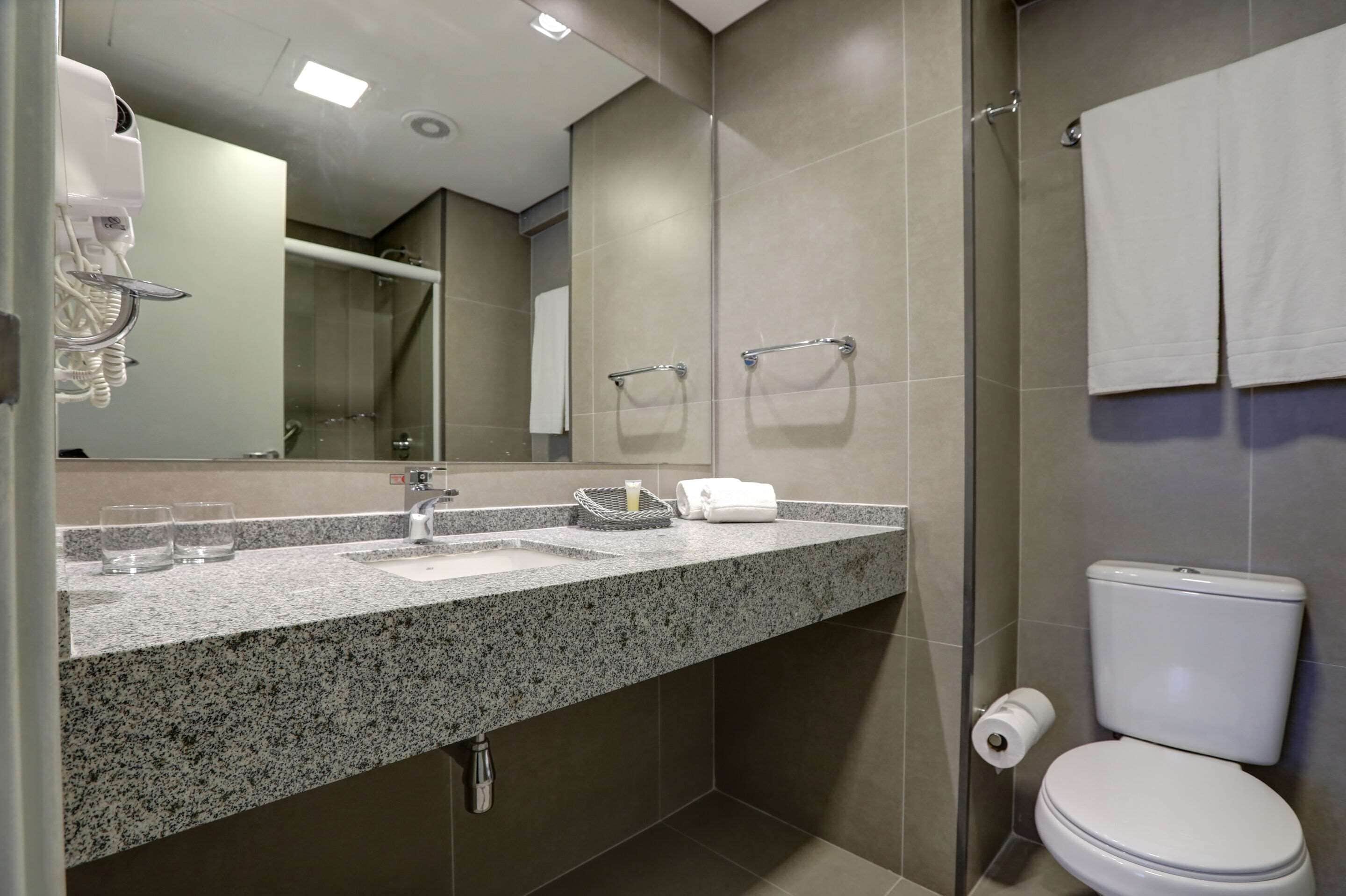 A modern bathroom with a granite countertop, a sink, a mirror, a toilet, and a shower area.