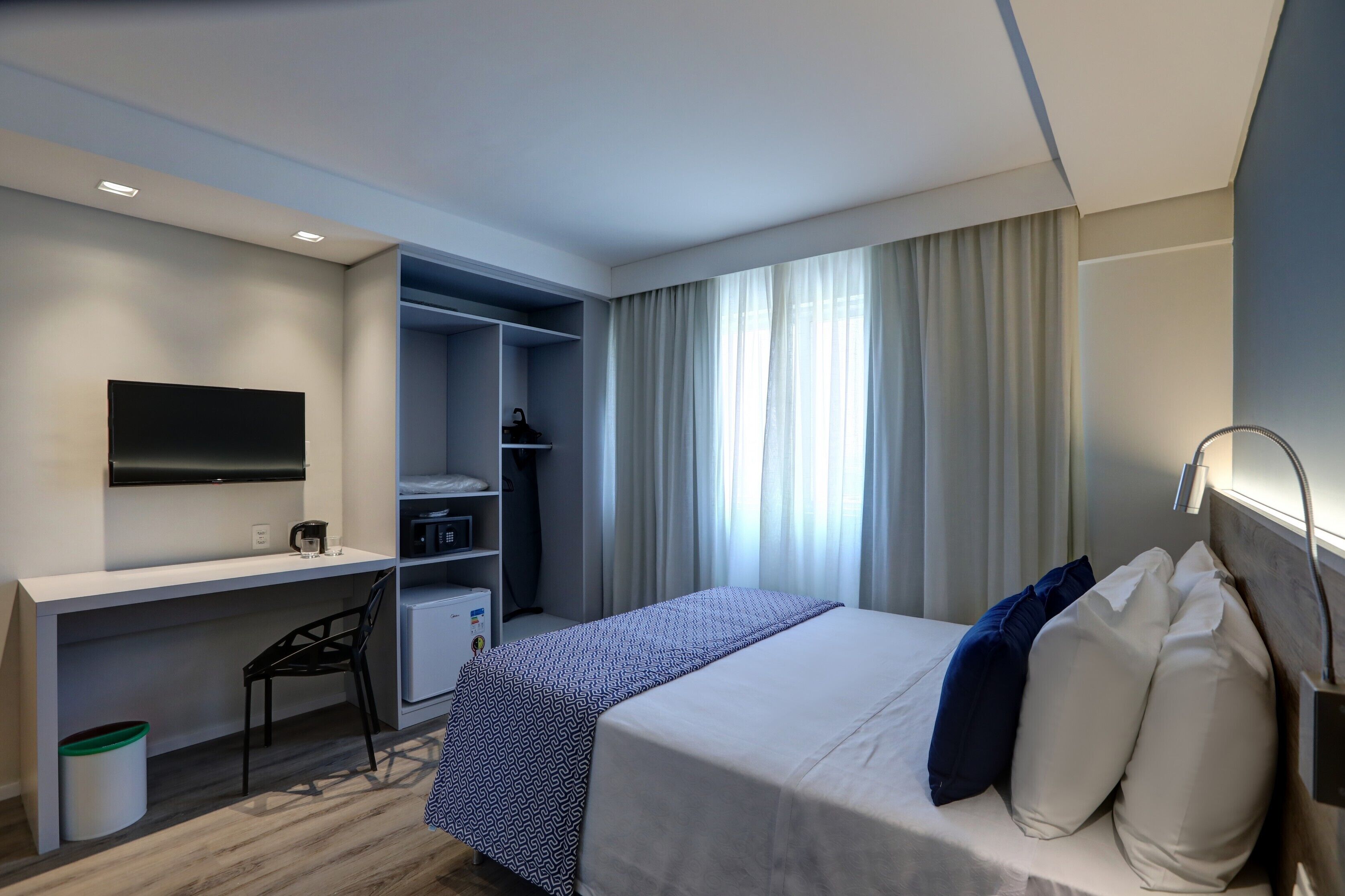 Een hotelkamer met een bed, een bureau, een stoel, een televisie en een kledingkast.