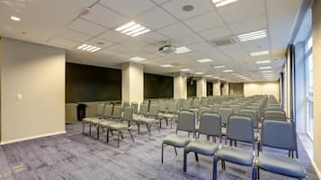 Un salón de conferencias con filas de sillas, un proyector y una pantalla grande.