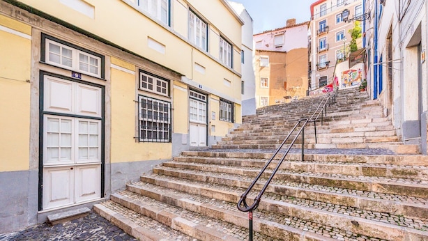 Unos escalones de piedra conducen a un edificio con una puerta blanca y ventanas con barrotes.