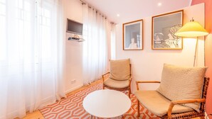 Una sala de estar con dos sillones de mimbre, una mesa de centro blanca y un televisor montado en la pared.