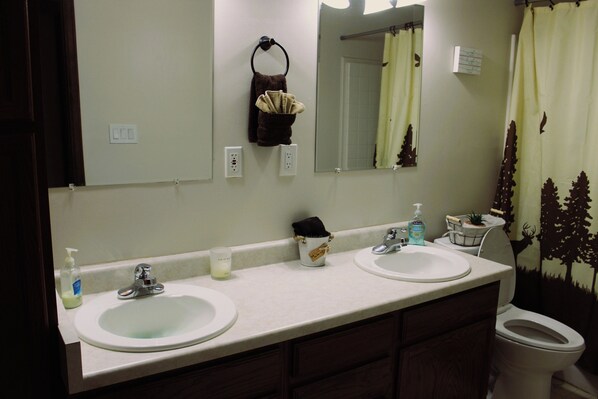 A bathroom with two sinks, a mirror, a toilet, and a shower curtain with a forest design.