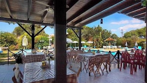 Une terrasse extérieure avec des tables et des chaises, une piscine et une vue sur la végétation environnante.
