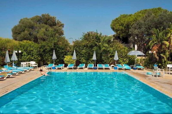 A swimming pool with lounge chairs and umbrellas, surrounded by trees. - Kassandra Apartments (Rhodes)