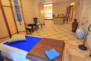 A hotel room with a checkered floor, a bed with a blue blanket, a patterned rug, a desk, a chair, and a vase with flowers. - Kassandra Apartments (Rhodes)