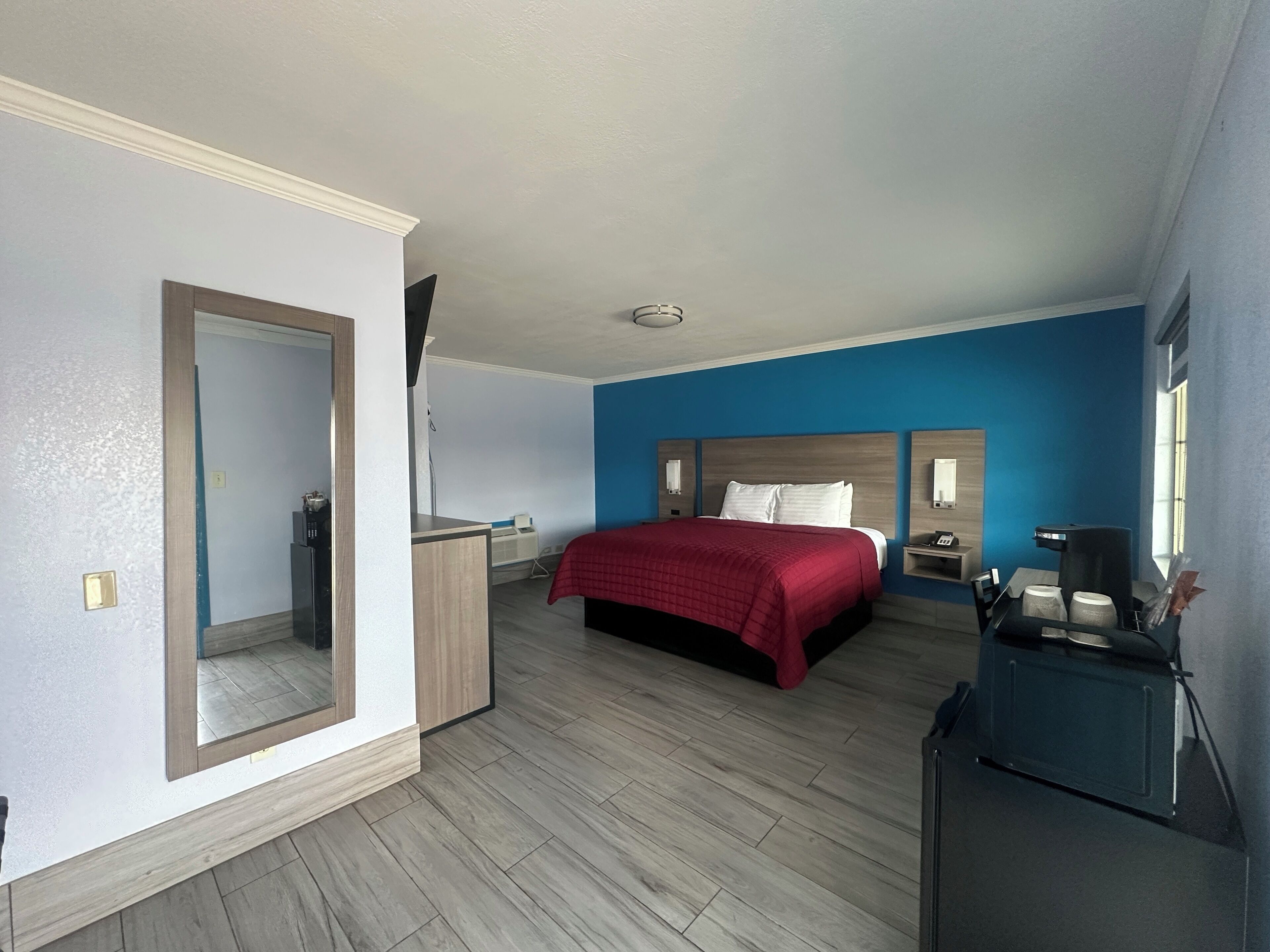 A modern hotel room with a large bed, a desk, a dresser, and a mirror.