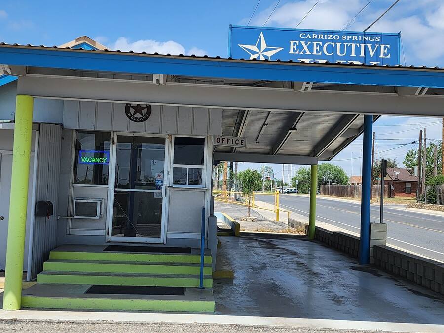 Um posto de gasolina Carrizo Springs com toldo azul, um aviso de 'Vagas' e um sinal de 'Bem-vindo'.