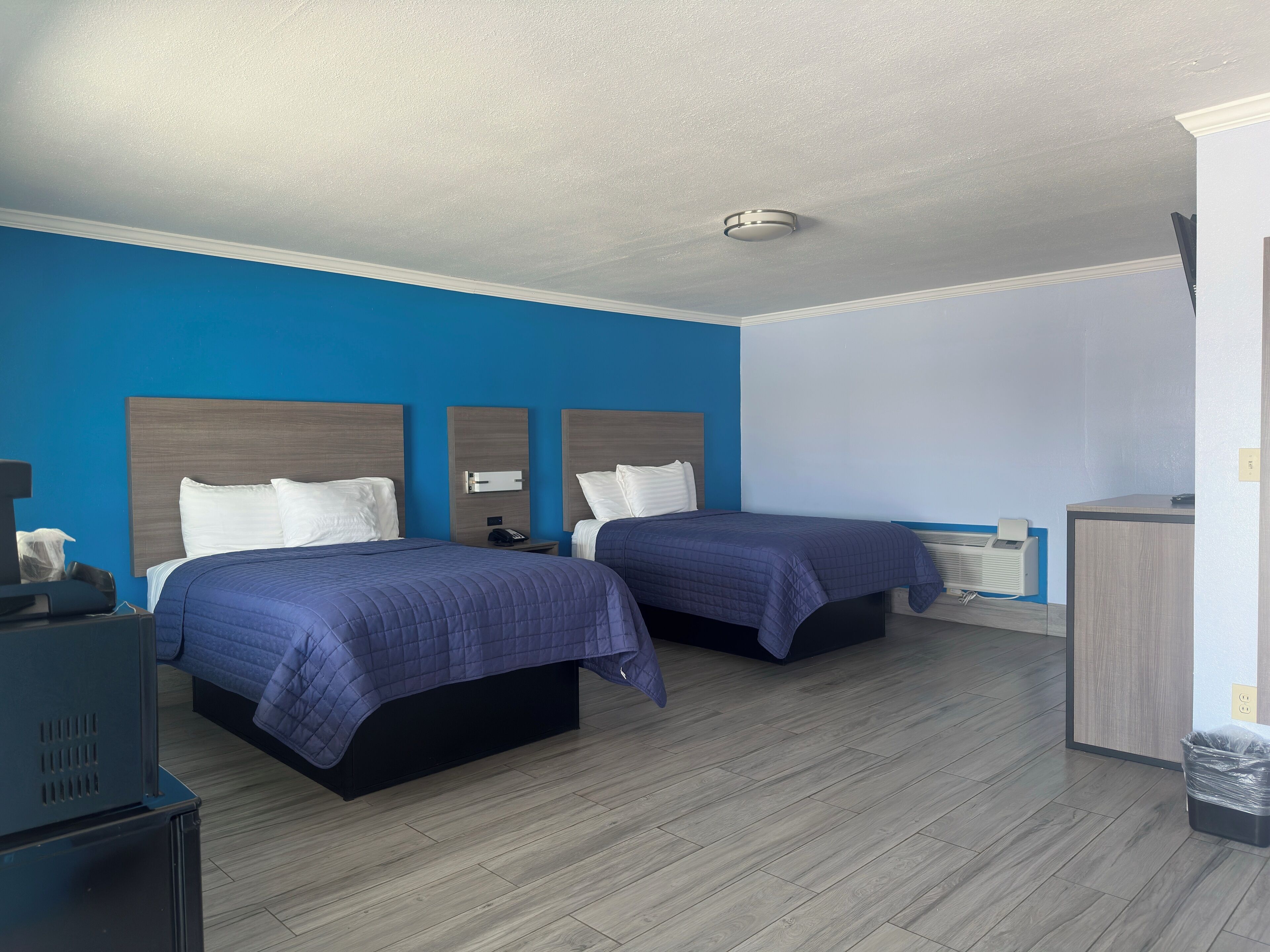 Une chambre d’hôtel avec deux lits, un bureau, une chaise, une poubelle et un radiateur.