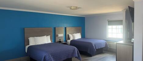 A hotel room with two beds, a desk, and a television.