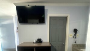A room with a wooden desk, a television mounted on the wall, a door, and a small trash bin. - Carrizo Executive Inn (Carrizo Springs)