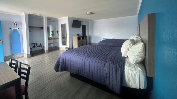 A bedroom with a large bed, a desk, and a chair. There is a bathroom visible in the background. - Carrizo Executive Inn (Carrizo Springs)