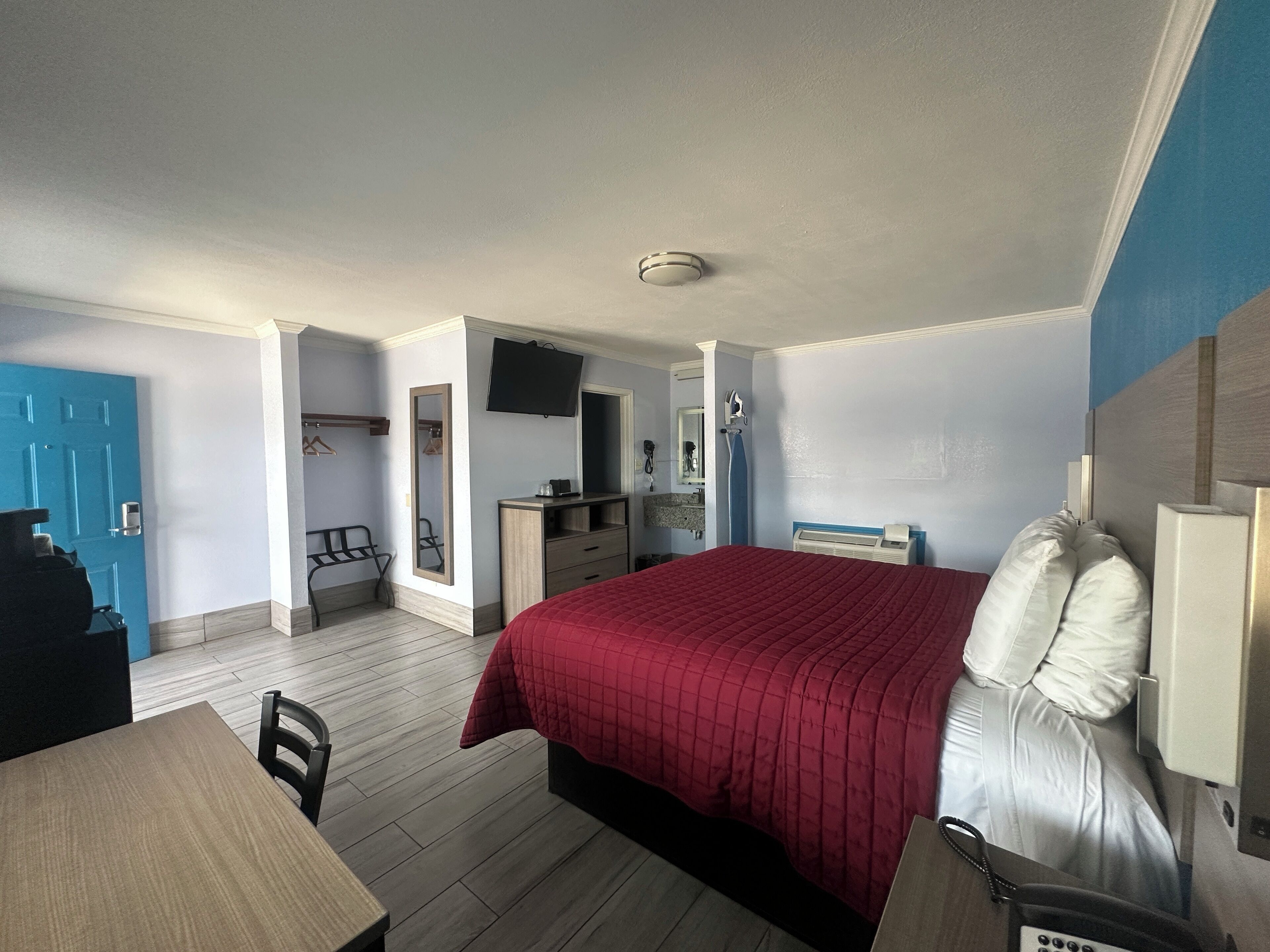 A hotel room with a bed, a desk, a chair, a mirror, a TV, and a bathroom.