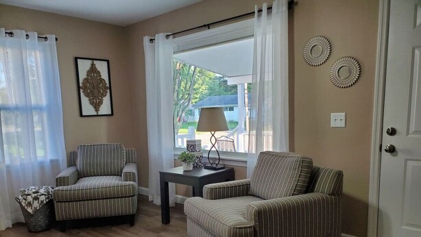 Una sala de estar con dos sillones a rayas, una mesita con una lámpara, un cuadro enmarcado y vistas a través de una ventana.
