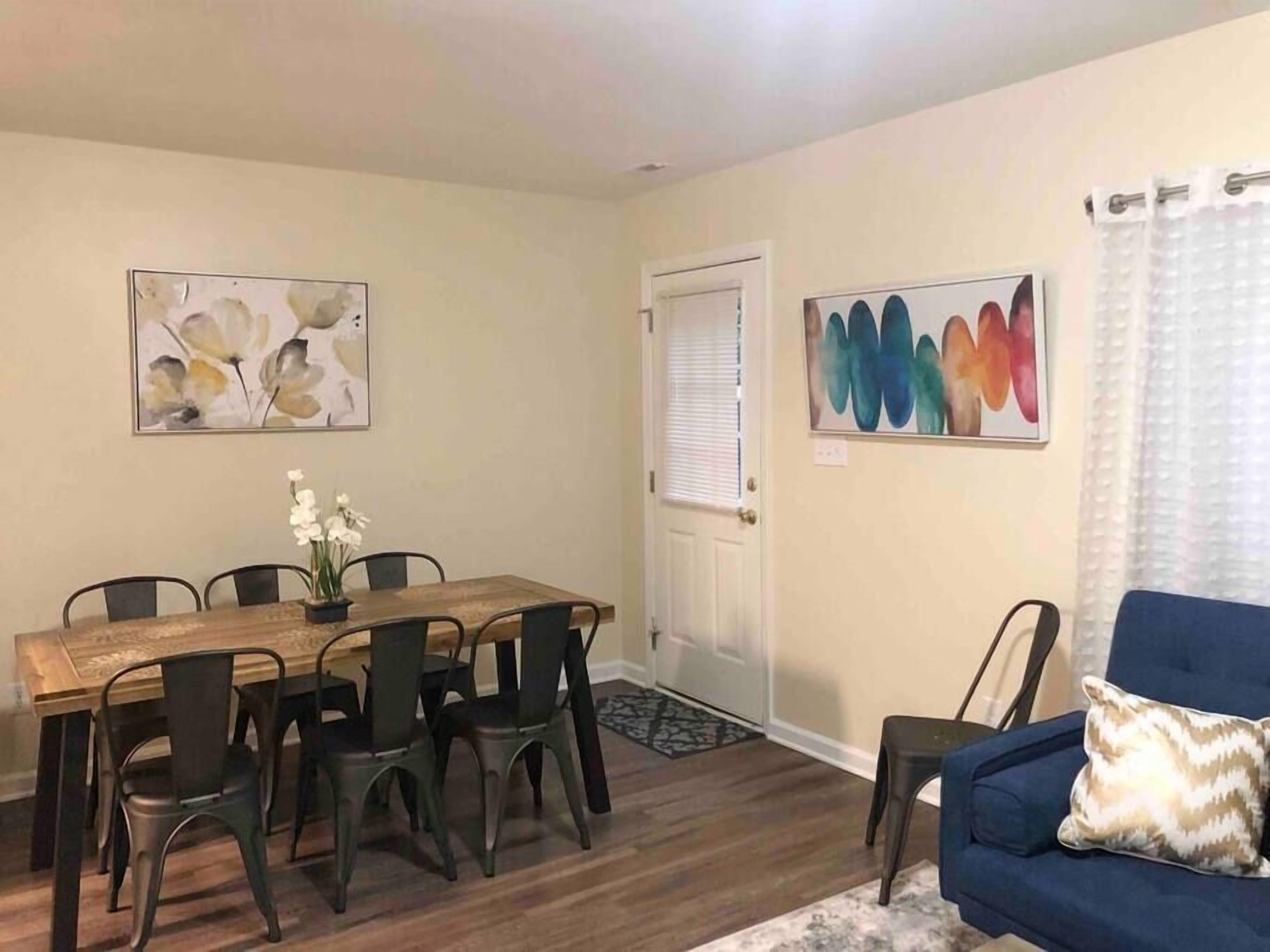 A dining area with a wooden table and chairs, a blue couch, and two abstract paintings on the walls.