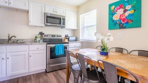 Een keuken met witte kasten, een magnetron, een oven en een eettafel met stoelen.