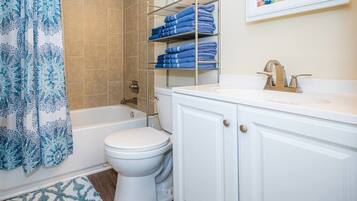 Une salle de bain avec des toilettes blanches, une baignoire, une douche et un porte-serviettes avec des serviettes pliées.