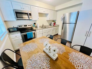 Une cuisine moderne avec des meubles blancs, des appareils en acier inoxydable et une table à manger en bois agrémentée de décorations centrales.