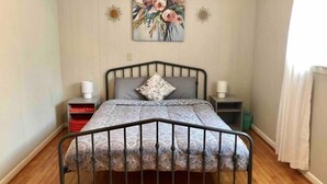 A bedroom with a metal bed frame, a floral painting on the wall, and a window with curtains.