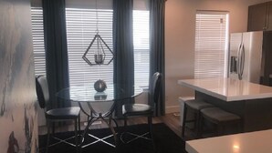 A modern kitchen with a dining area, featuring a round table, chairs, and a hanging light fixture.