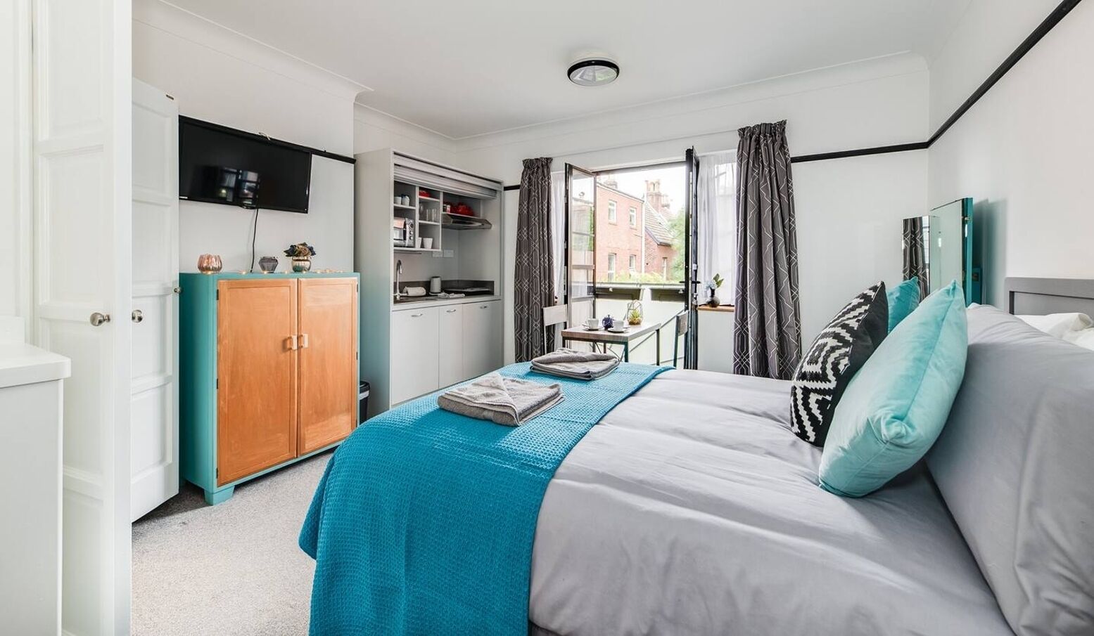 Ein Schlafzimmer mit Bett, Kleiderschrank, Schreibtisch und einem Fenster mit Vorhängen.