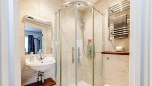 Un baño moderno con ducha envuelta en vidrio, un lavamanos blanco y un perchero para toallas.