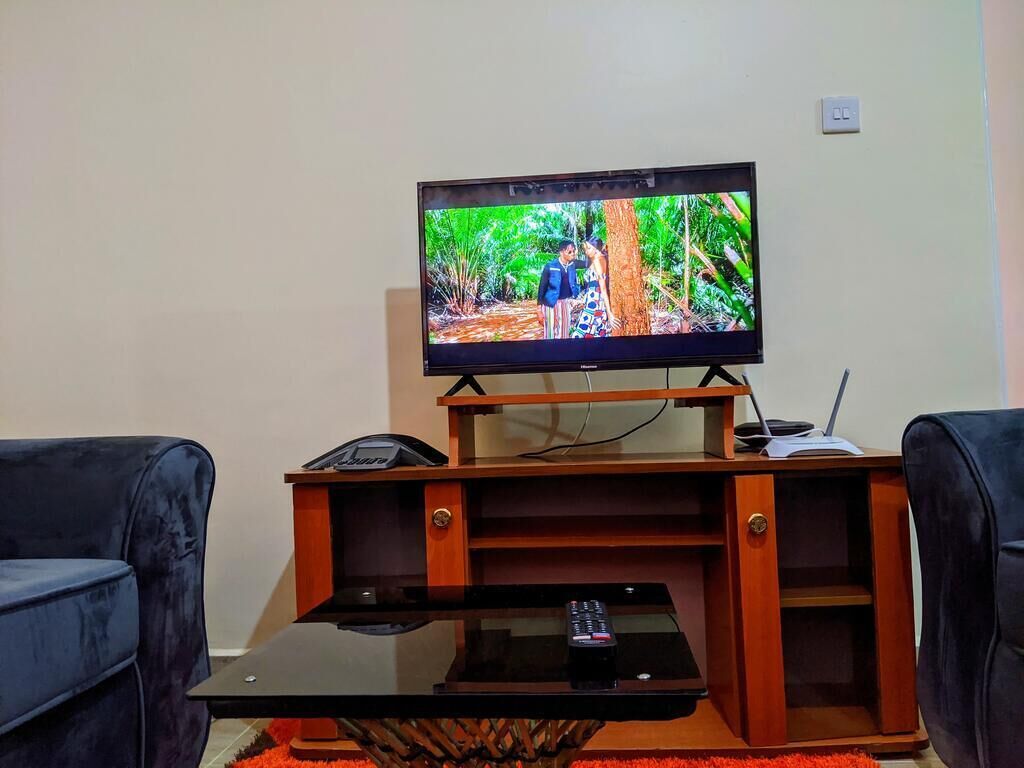 A television on a wooden stand with a remote control on a glass table in front.
