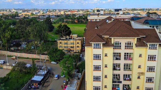 Un edificio residenziale a più piani con balconi, un'area di parcheggio e vista sullo skyline urbano.