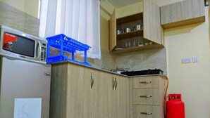 Una cucina con forno a microonde, cesti portaoggetti blu, mobili in legno, piano cottura a gas e bombola di gas rossa.