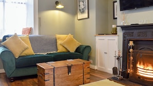 Un salon chaleureux avec un canapé vert, une commode en bois, une cheminée et un téléviseur.