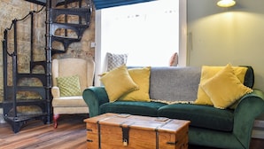 Un salon chaleureux avec un canapé vert, une commode en bois et un escalier en colimaçon.