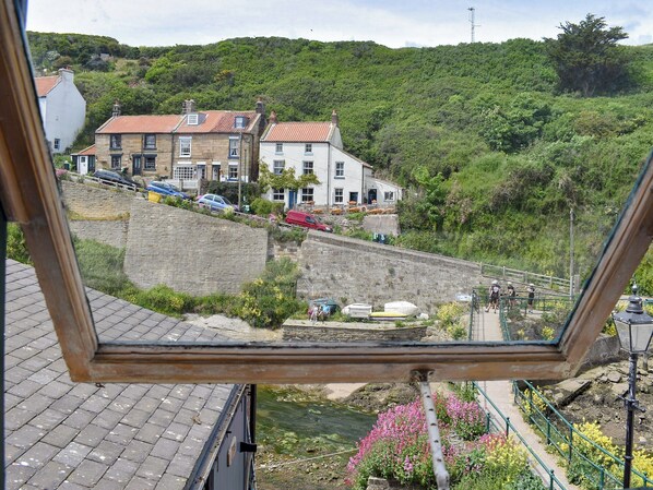 A view from a window overlooking a hillside with buildings, a stone wall, and a pathway with people walking.