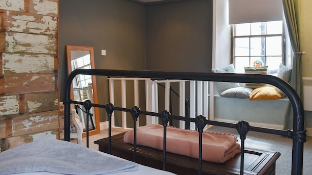 Une pièce avec un mur en bois rustique, un berceau avec un matelas rose, une fenêtre avec des rideaux et un luminaire suspendu.