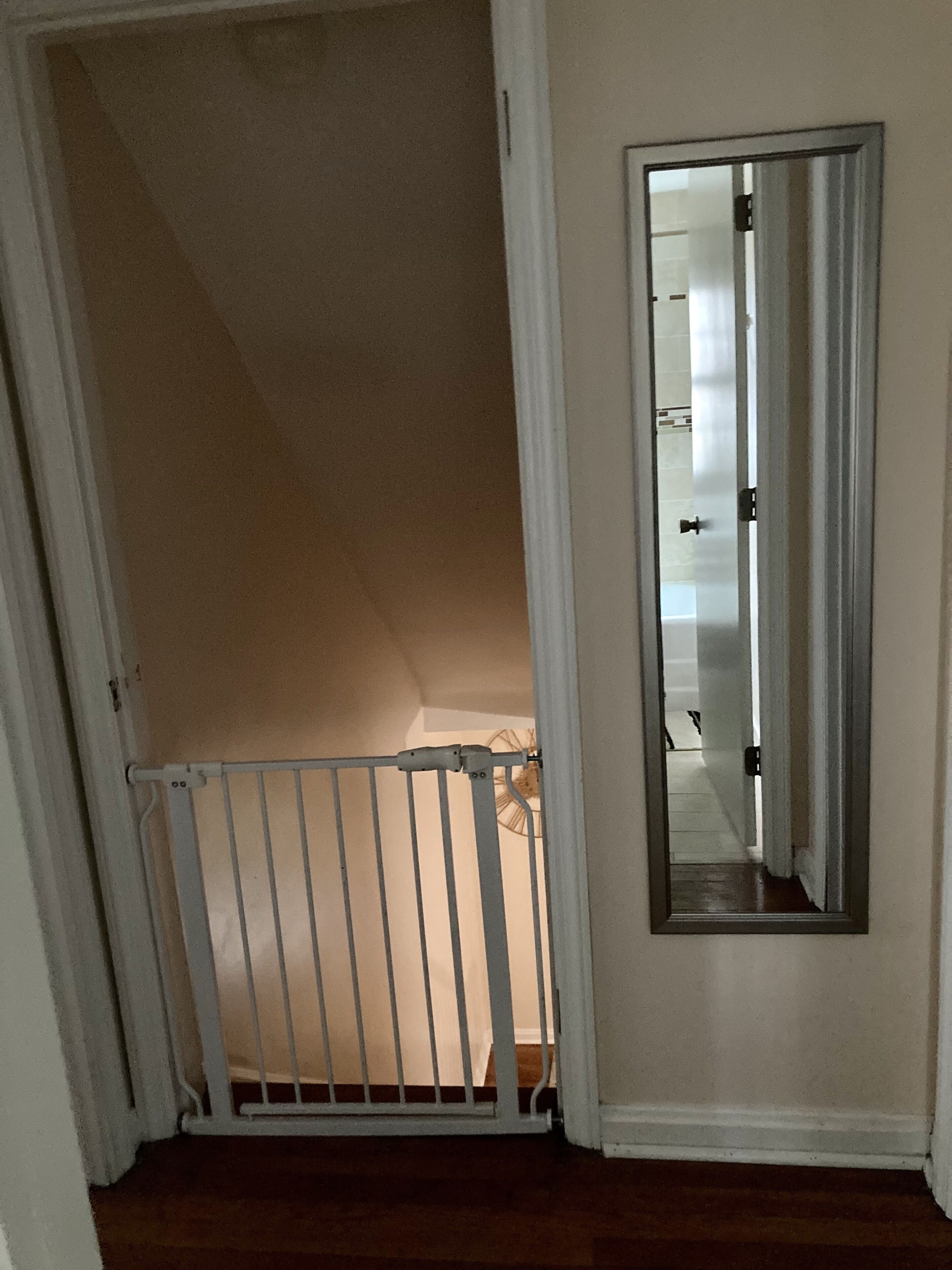 Een smalle trap met een witte leuning die uitkomt op een plateau. Een spiegel hangt aan de rechterkant aan de muur.